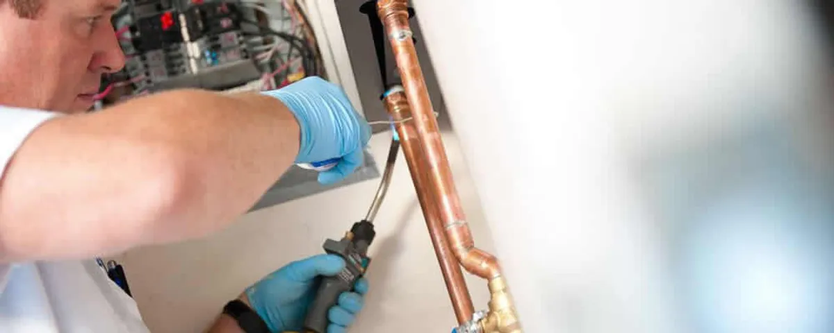 Water heater repair technician testing copper pipe connections and controls in Loveland, CO